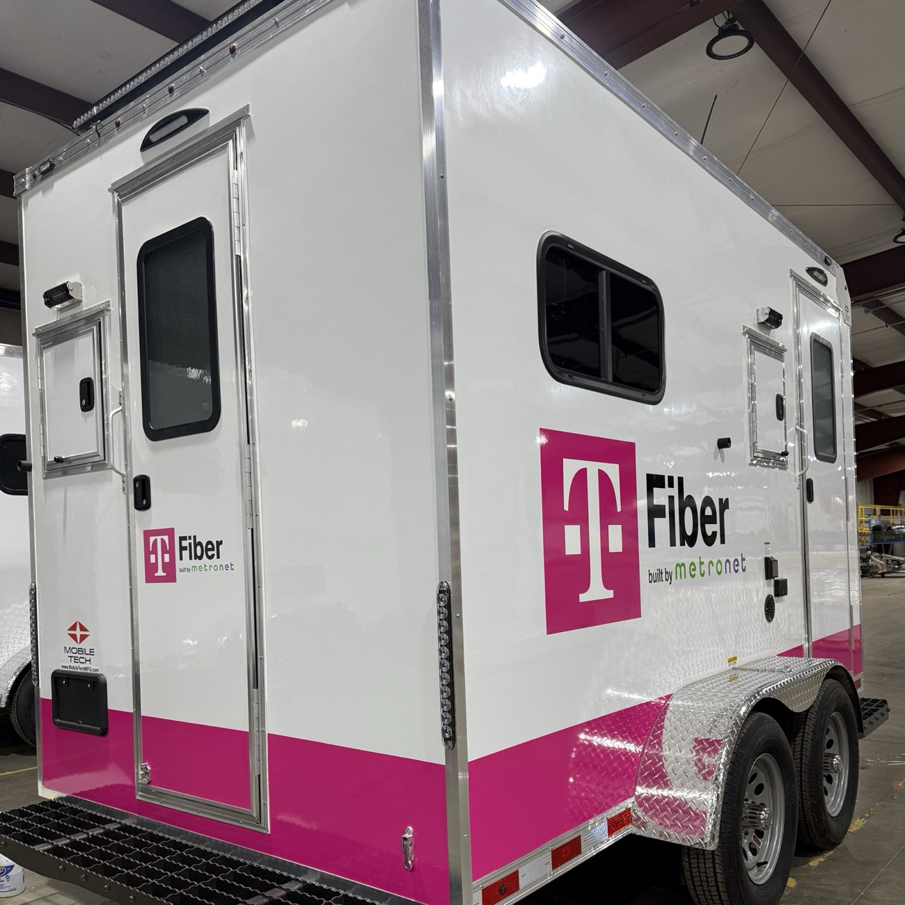 Mobile trailer wrapped in T-Mobile Fiber branding with magenta accents.