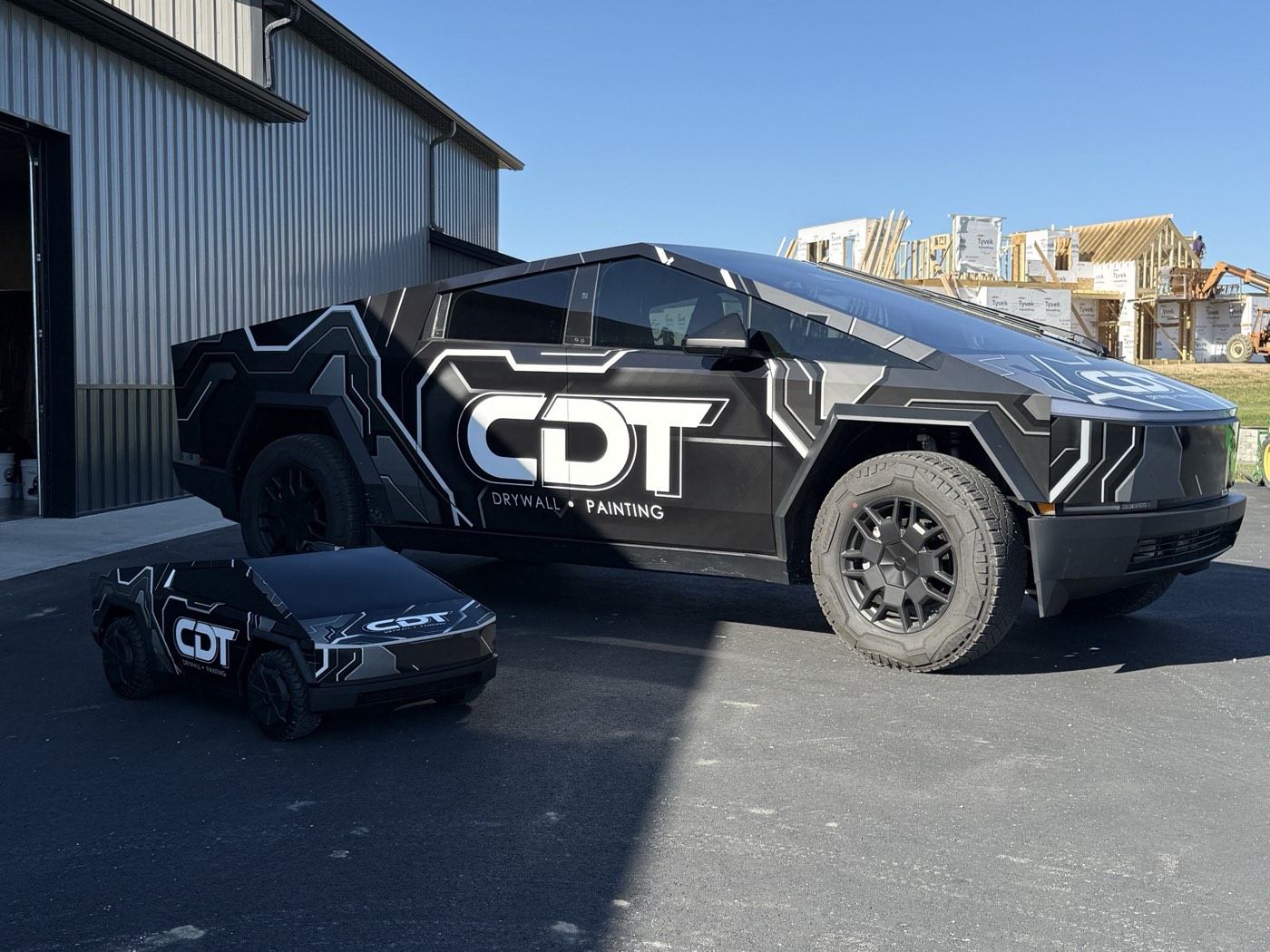 Cybertruck wrapped for CDT Drywall & Painting beside a matching mini Cybertruck.